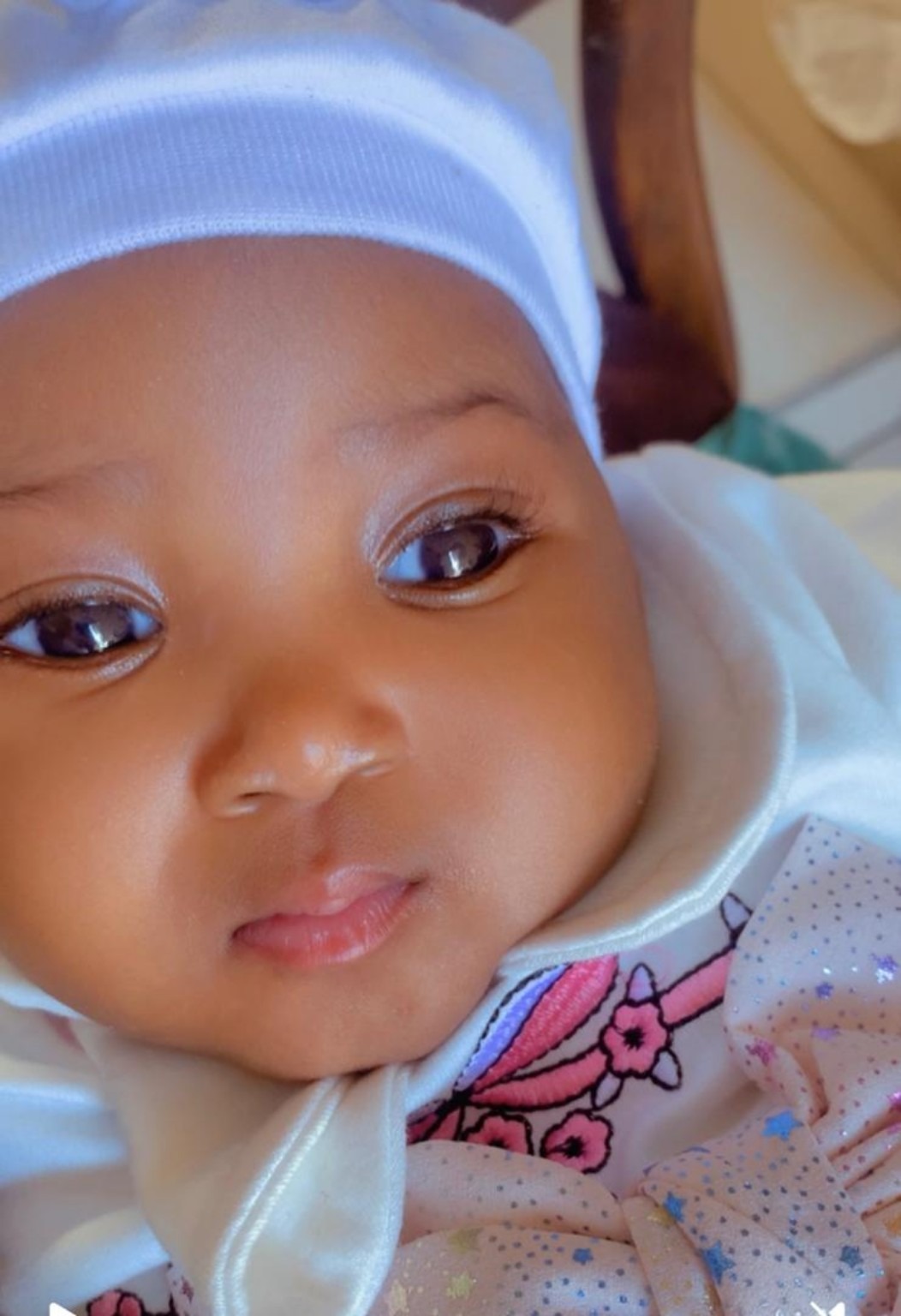 Close-up of a baby girl in a white cap, looking toward the camera.